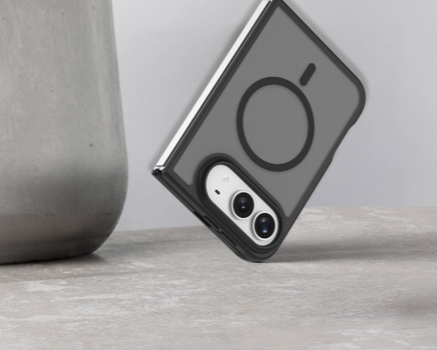 A dark gray MagSafe-compatible iphone ultra case with a black camera ring, shown on a smartphone, resting on a light gray textured surface next to a gray ceramic vase.